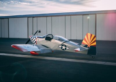 Photo of an RV-7 which is a small silver aircraft with a black and white checkered nose.